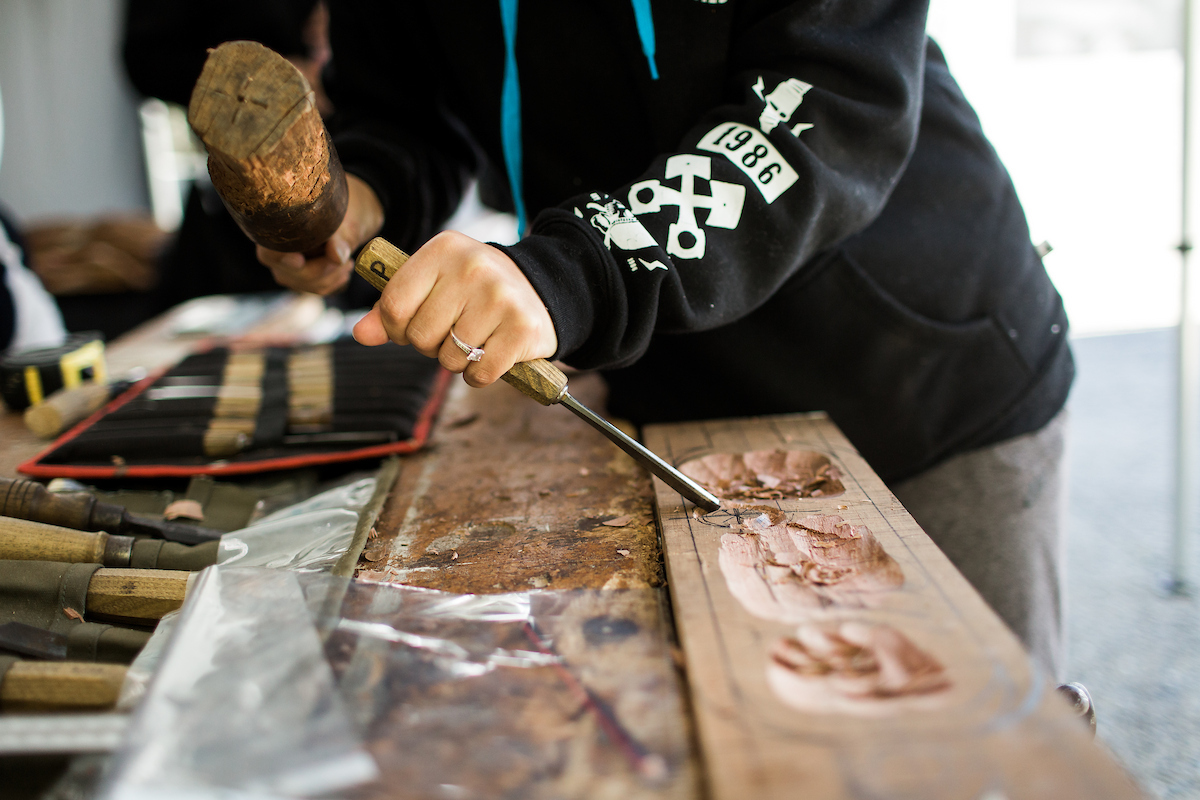 The hands of a person carving whakairo wooden artwork
