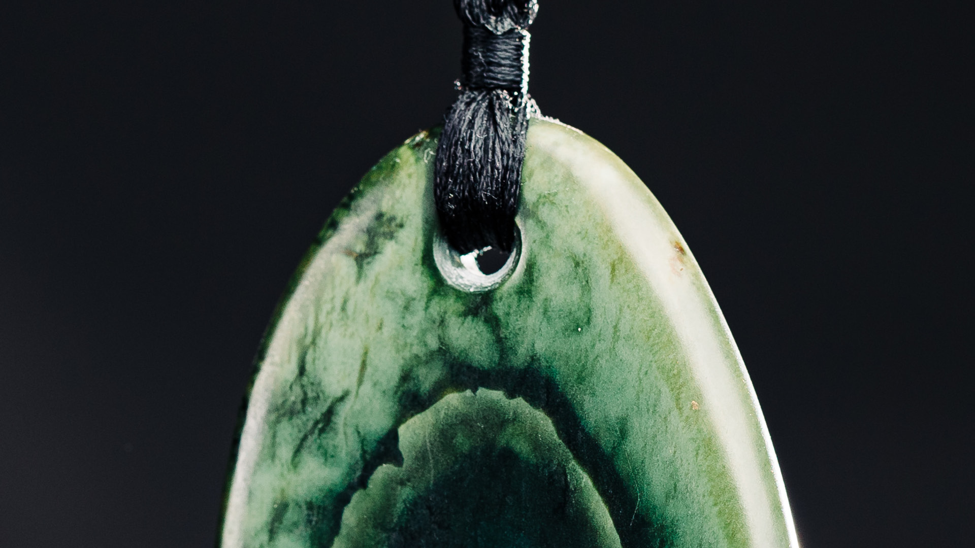Pounamu pendant on black string in front of a black background