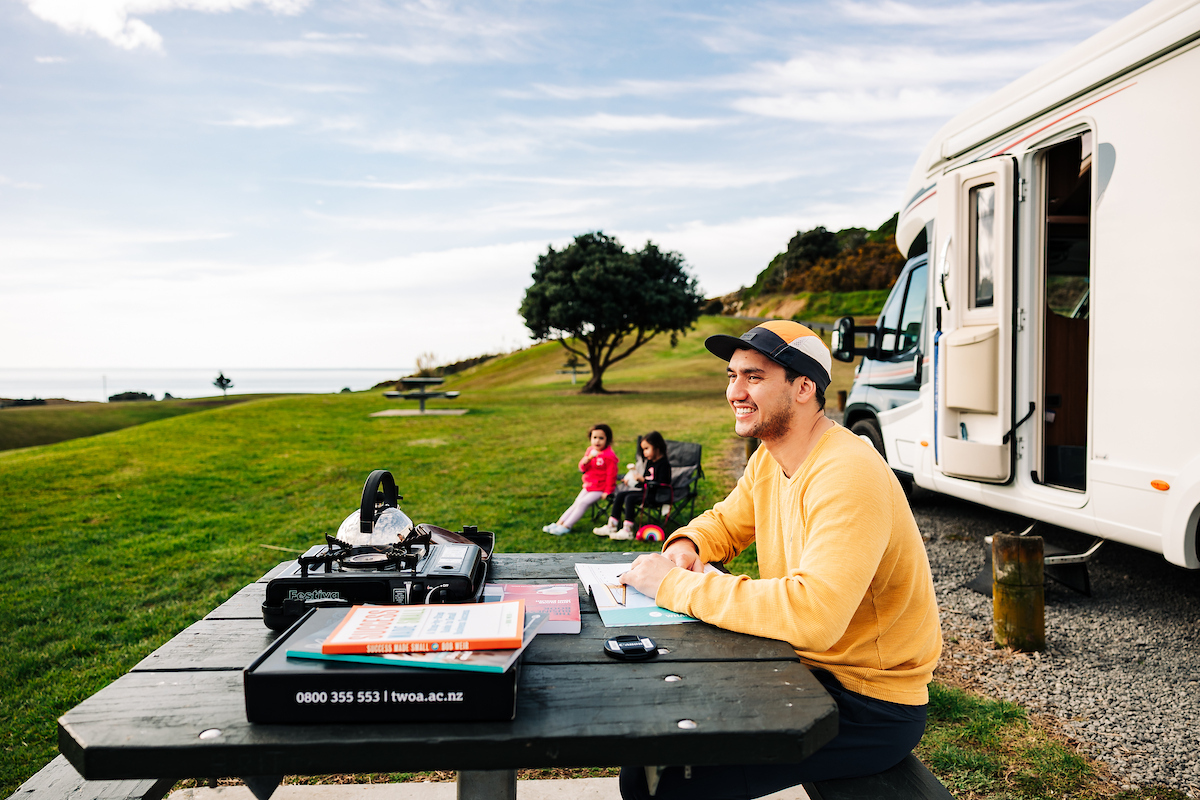 A man studies te reo Māori while on holiday with a campervan by the beach
