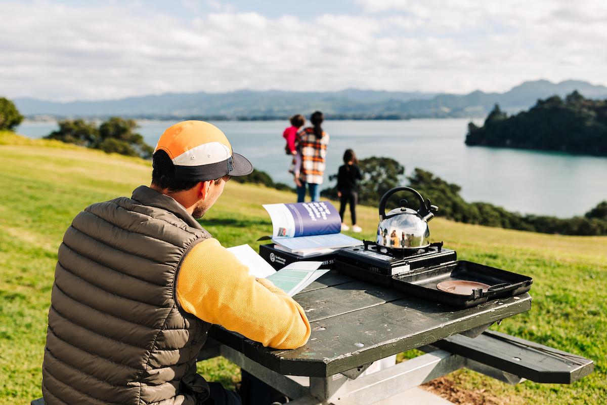 A man studies te reo Māori at a picnic table by the beach