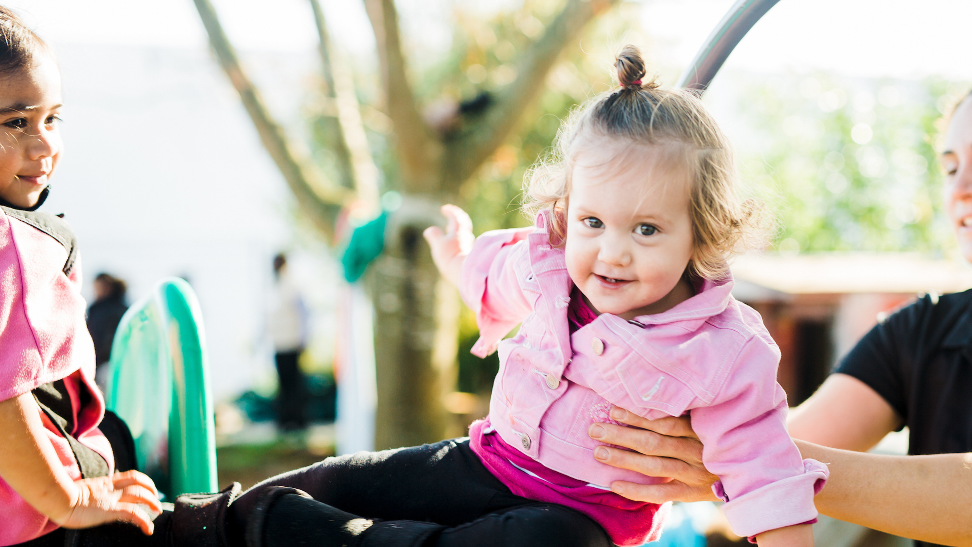 ELC teacher supporting child in pink top on playground