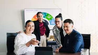 Four professionals in a boardroom present their slideshow