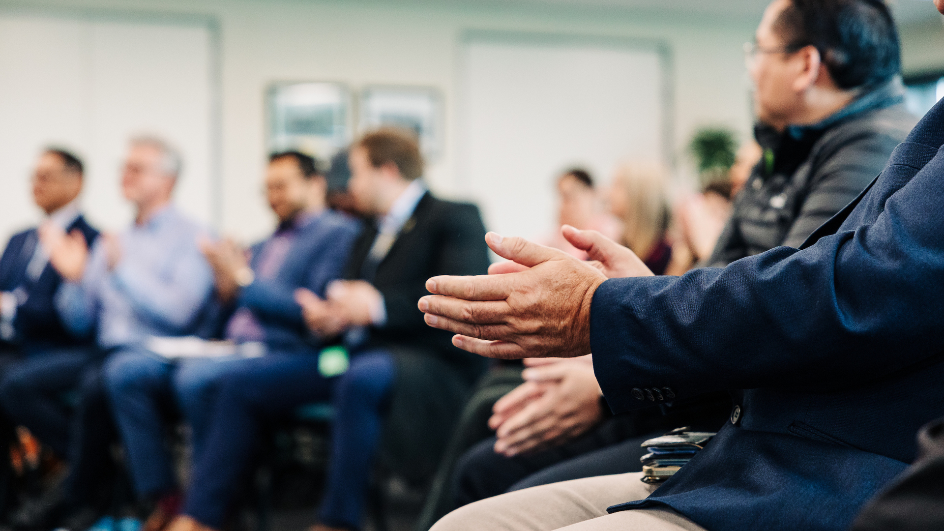 A seated audience in business attire are clapping