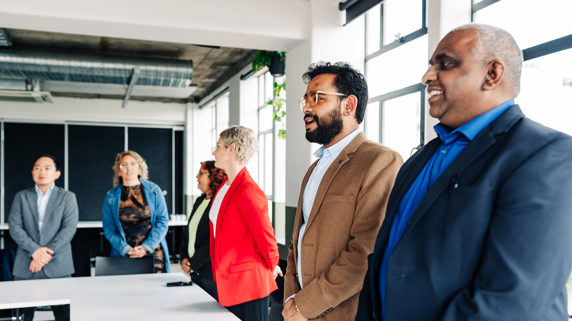 Professionals wearing business attire stand in a boardroom for karakia