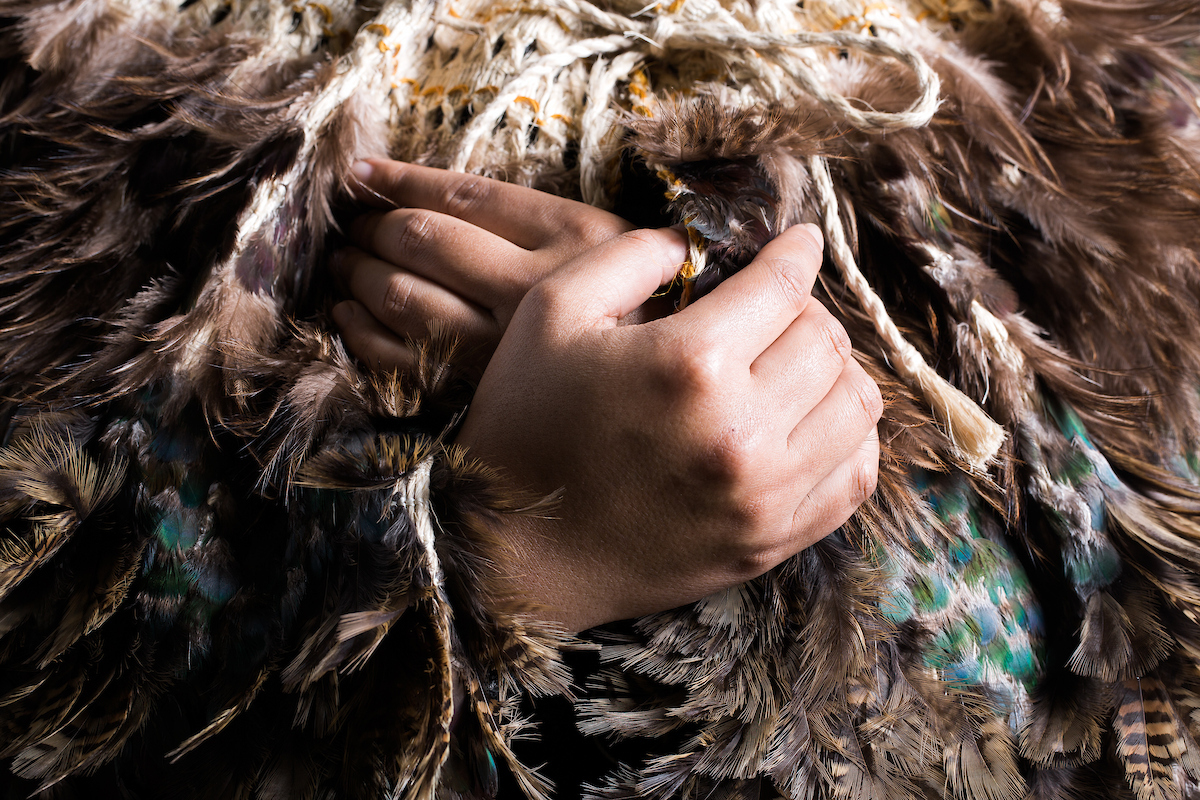 Two hands clasp a korowai cloak together