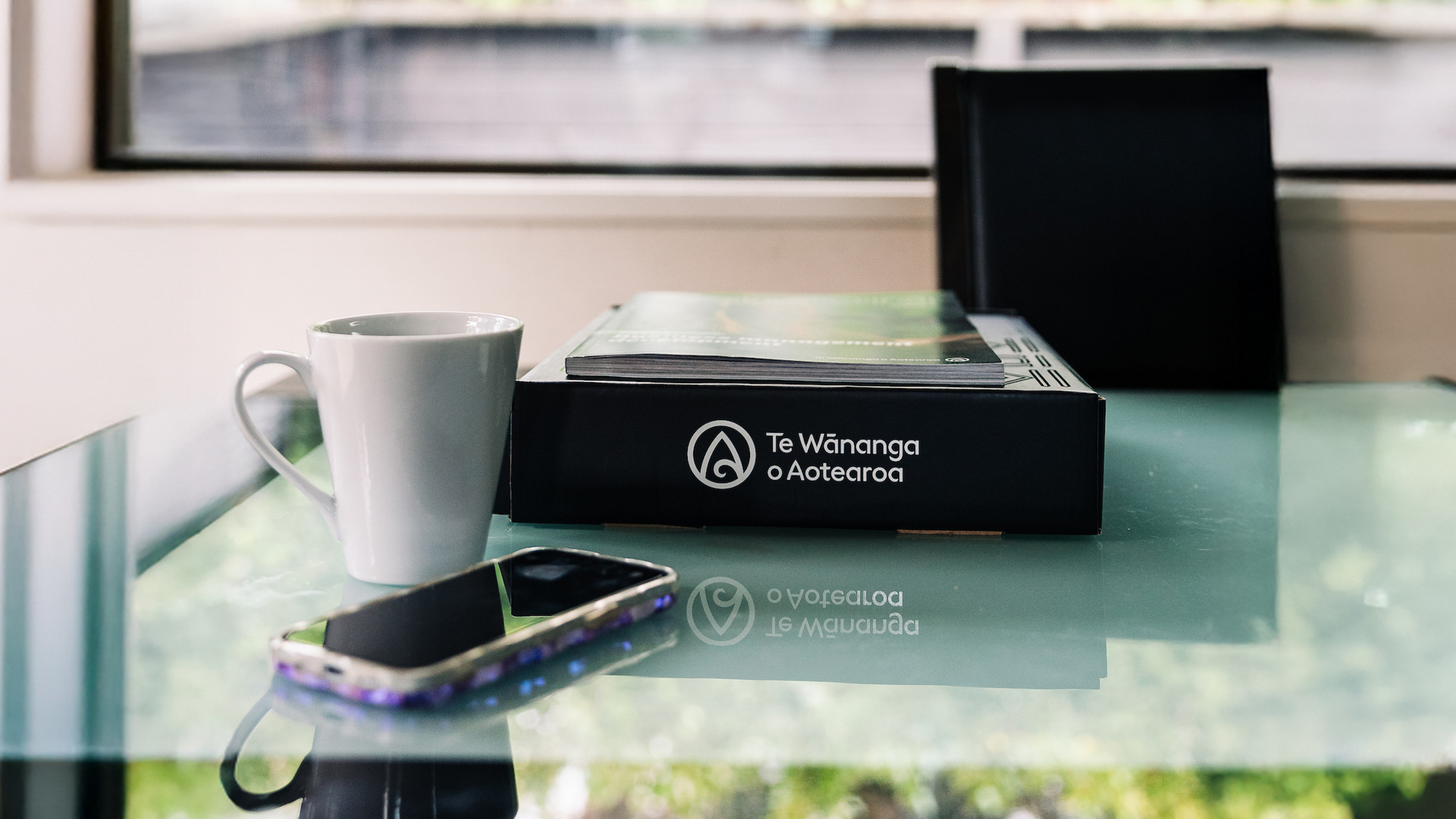 A black box of learning resources, a coffee cup and a mobile phone sit on a dining table