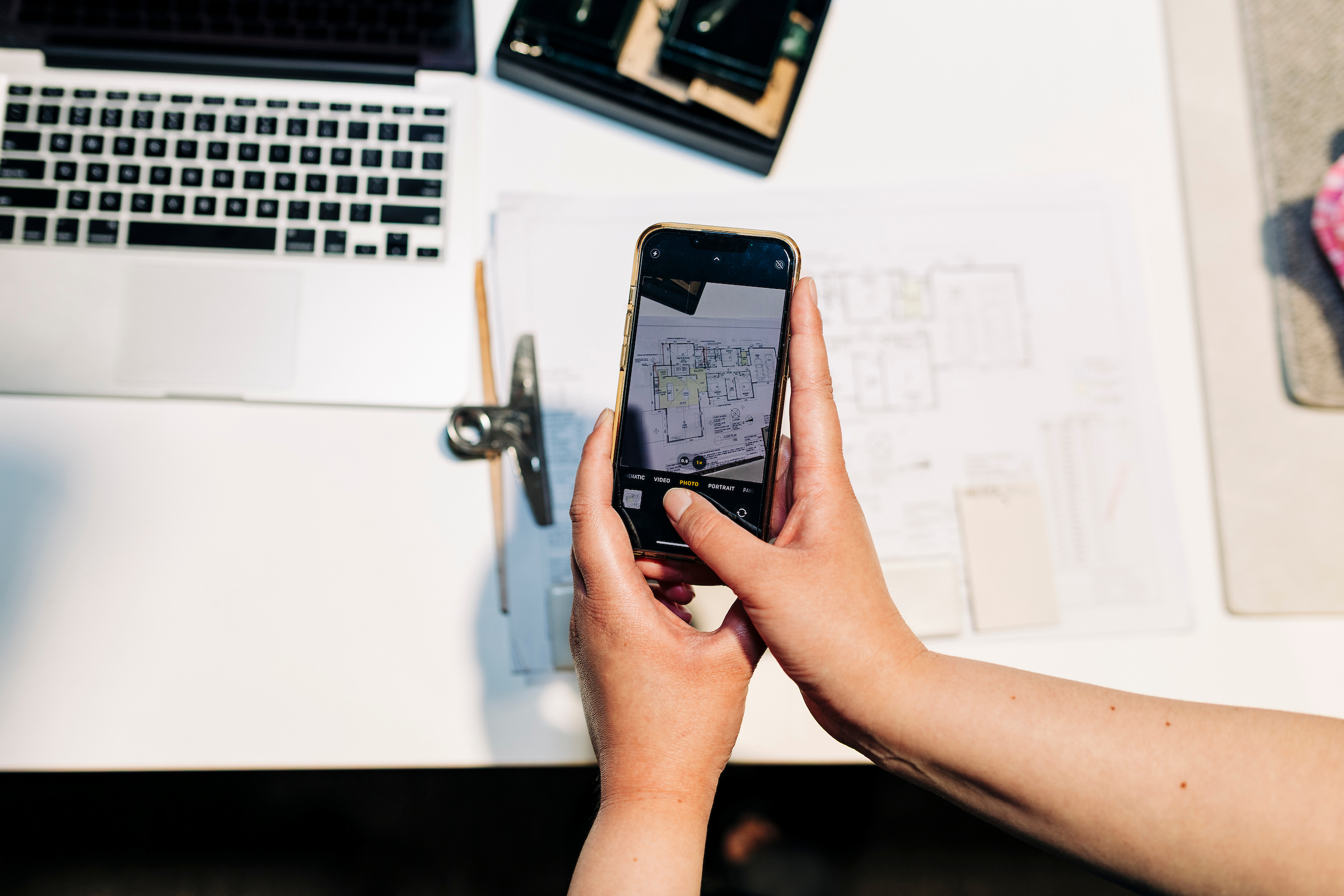 A view of someone's hands as they take a photo of a floorplan on their phone, a laptop in the background