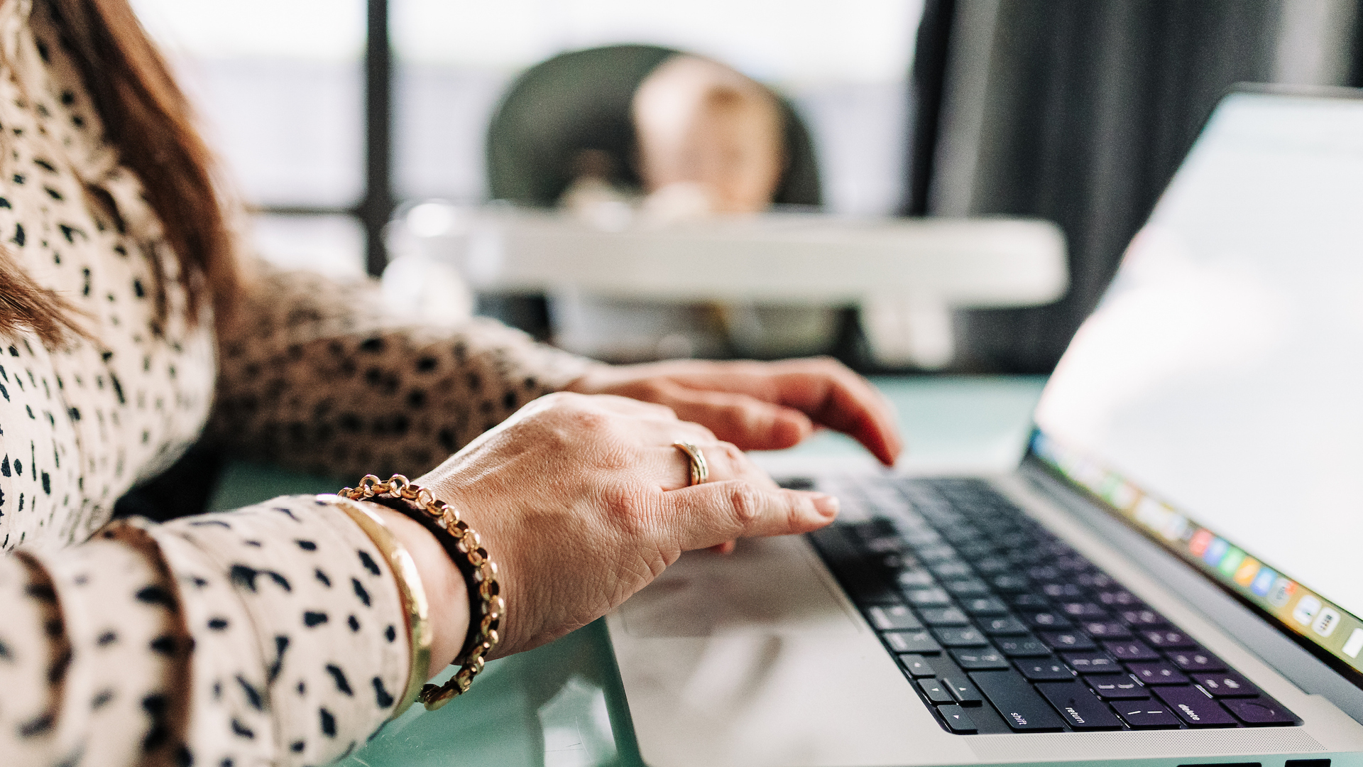 A woman studying at the dining table with her baby in the highchair