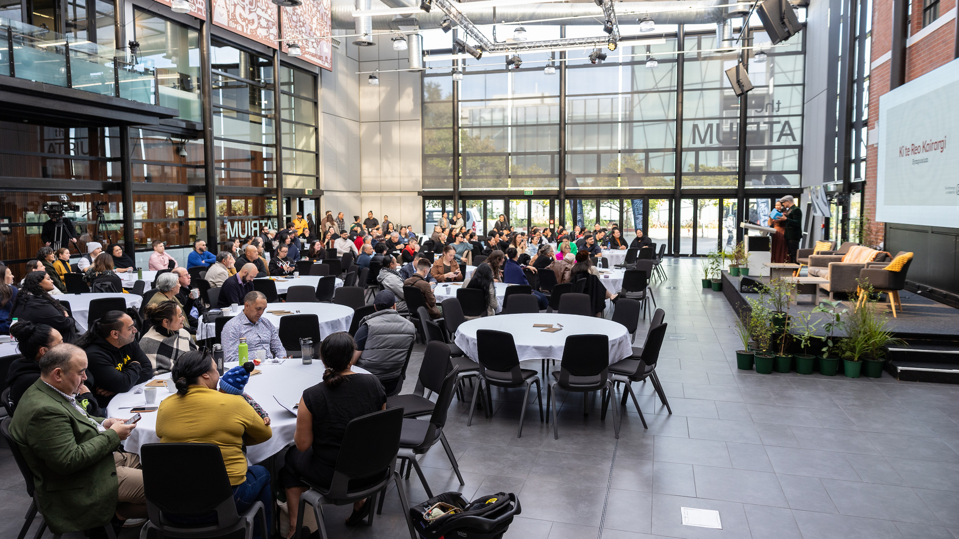 Groups of people at an event sit at round tables in an atrium