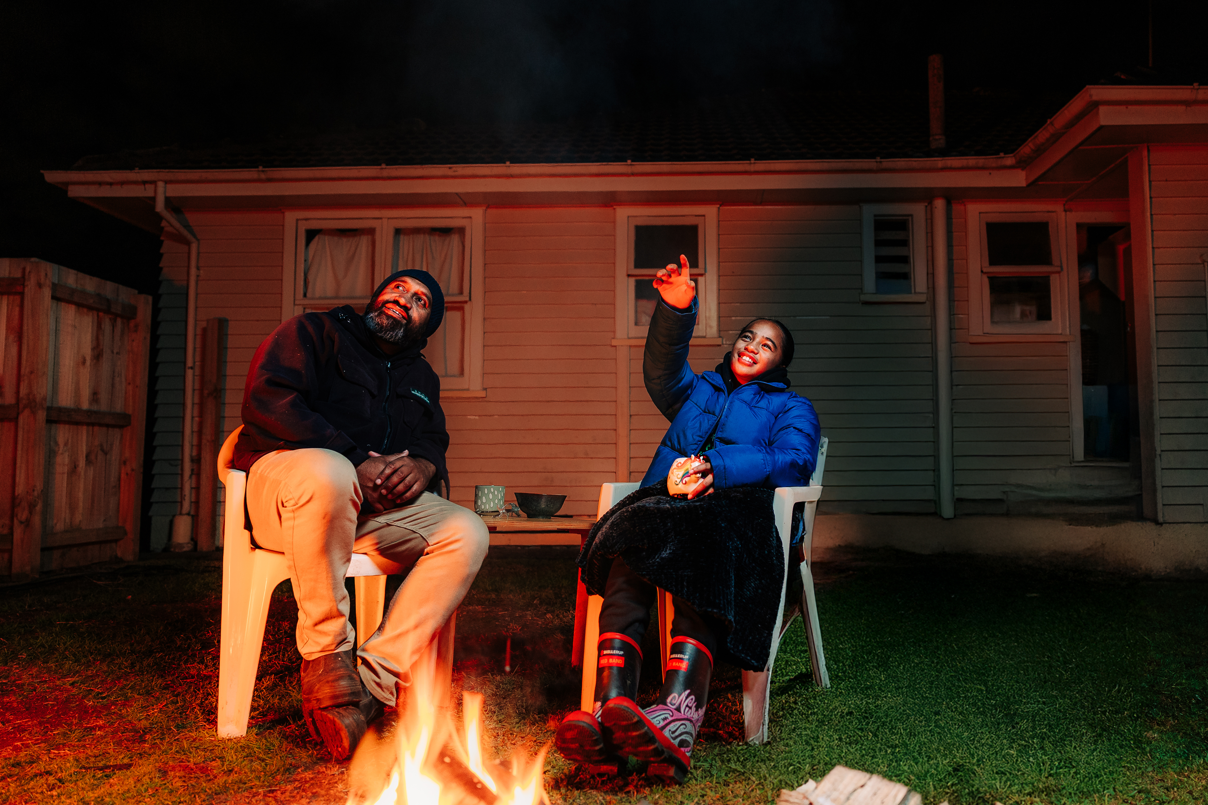 A father and daughter sit by a fire at night and look at the sky