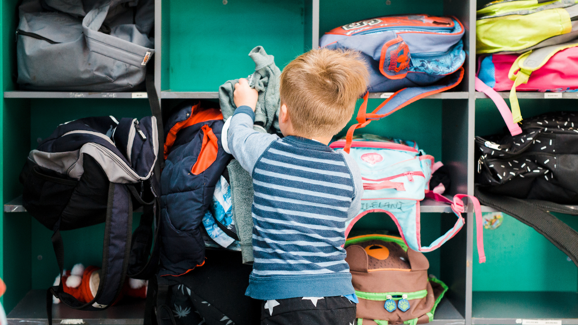 Child putting school bag in cubby hole 