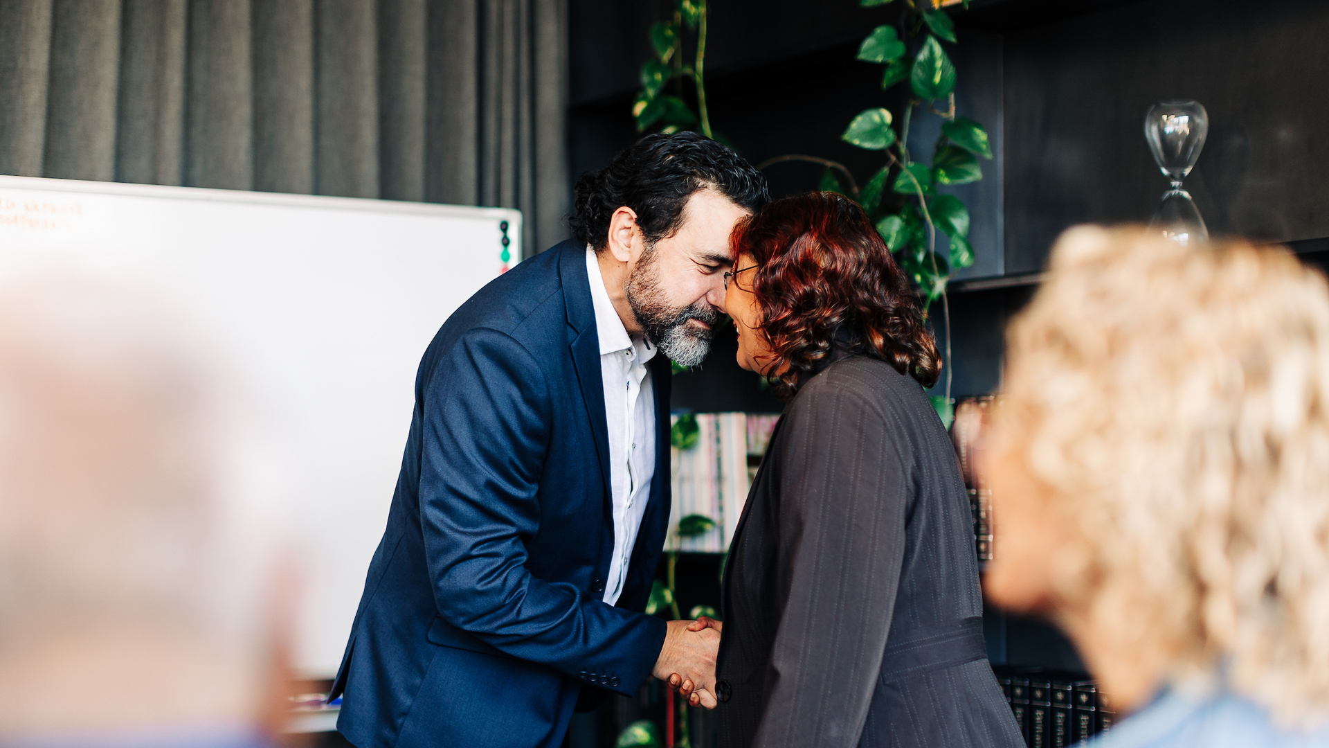 A close up view as two people hongi in front of a board room