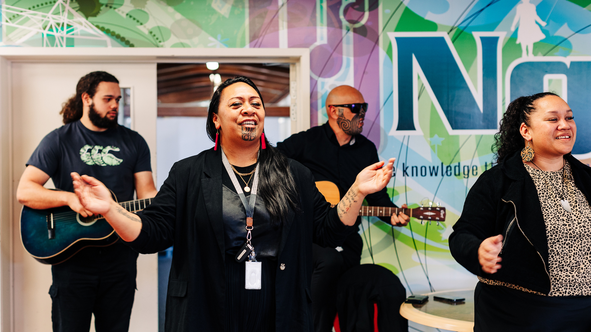 A group play guitar, sing and dance at the front of the room
