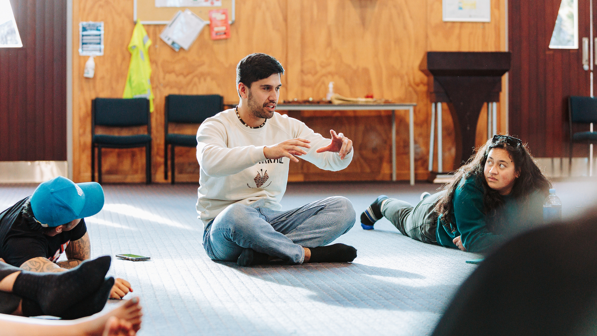 A group of students sit on the carpet while a man describes something with hand gestures