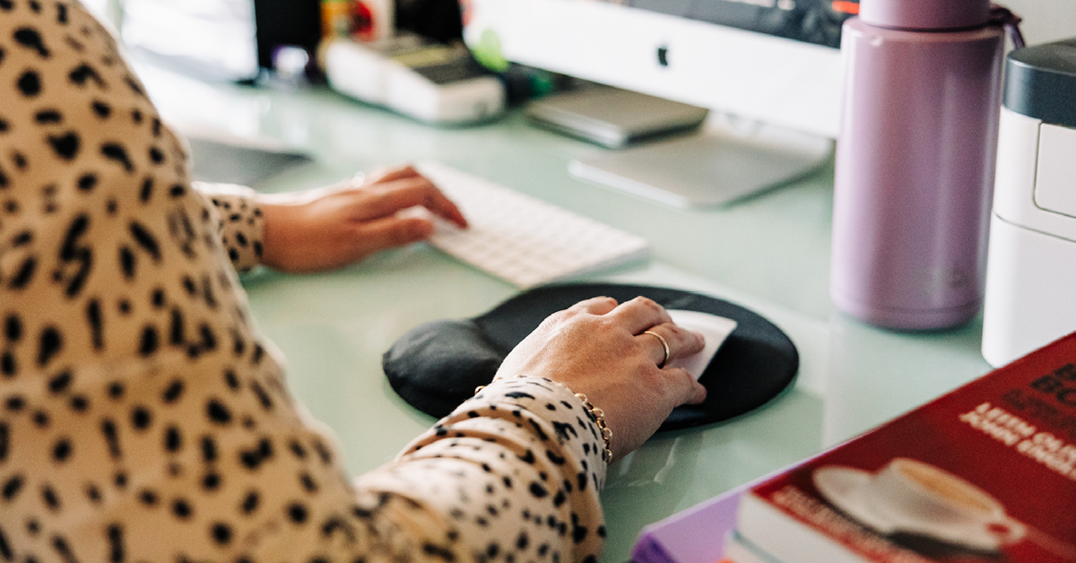 A close up of a woman's hands as she is using a computer at her desk